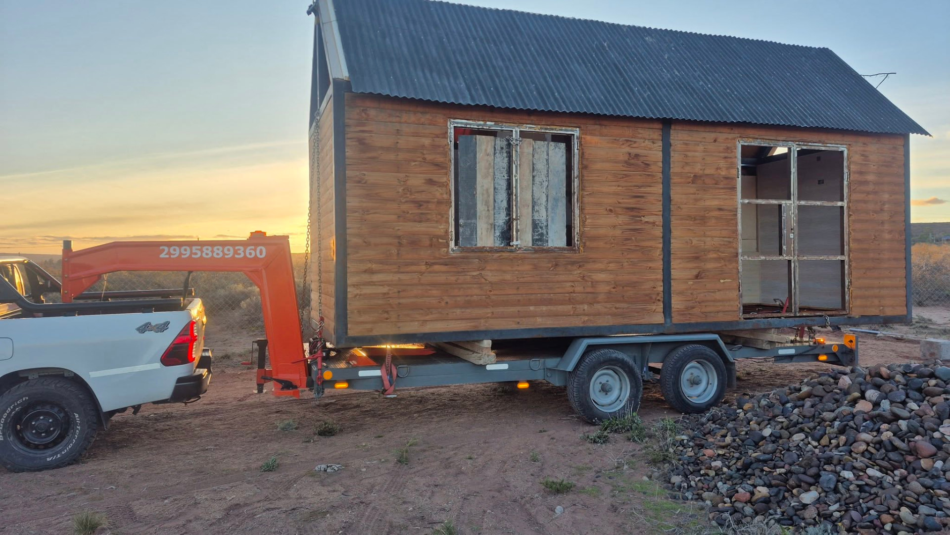 Traslado de una casilla de madera sobre trailer al atardecer